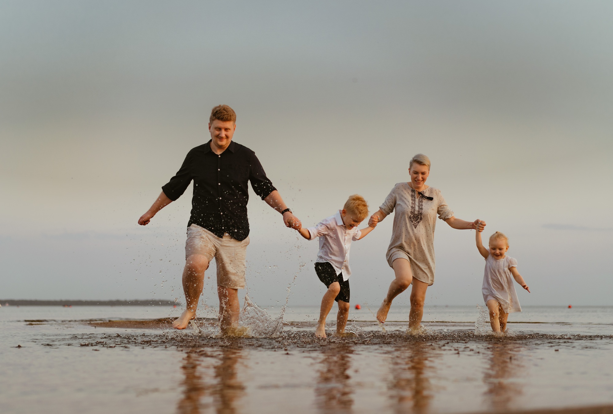 bonita familia caucásica divirtiendose corriendo en el mar al atardecer.vacaciones de verano con niños